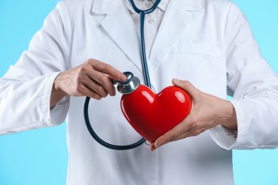 Doctor with stethoscope and red heart on light blue background, closeup