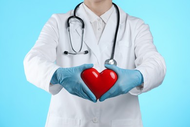 Doctor with red heart on light blue background, closeup