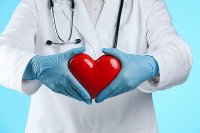 Photo of Doctor with red heart on light blue background, closeup