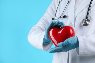 Photo of Doctor with red heart on light blue background, closeup. Space for text