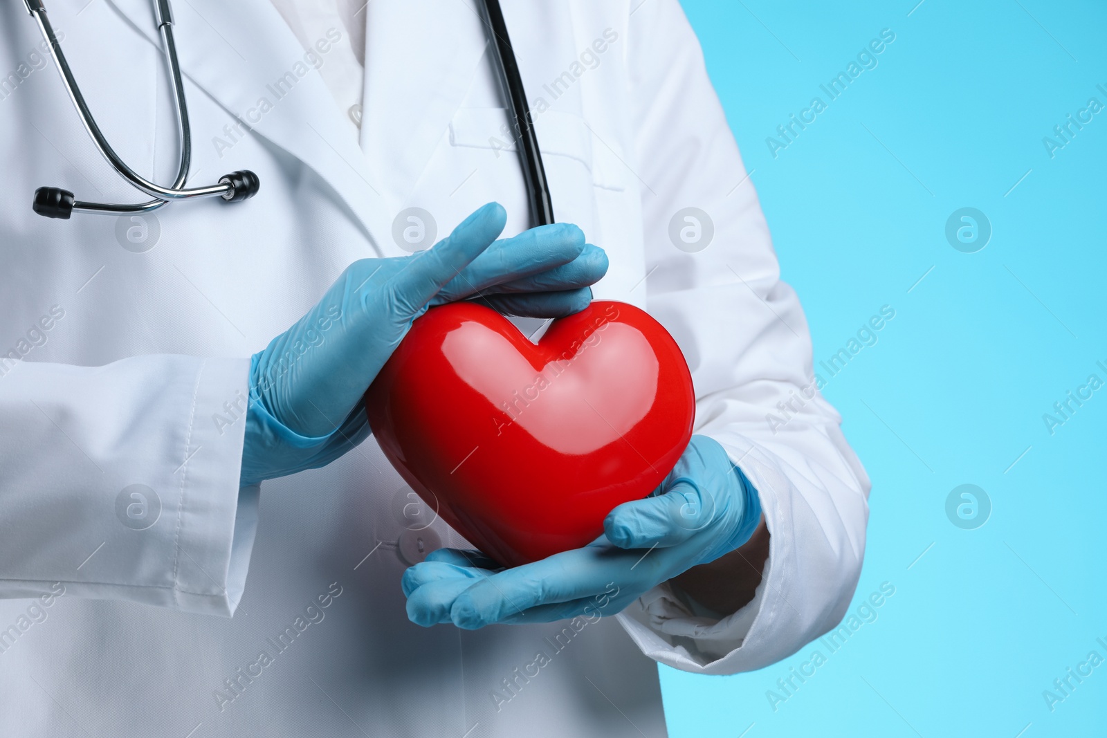 Photo of Doctor with red heart on light blue background, closeup