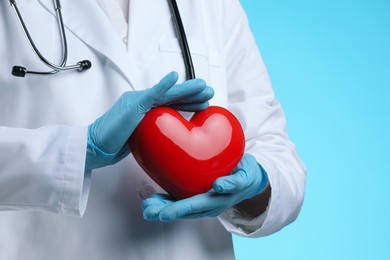 Doctor with red heart on light blue background, closeup