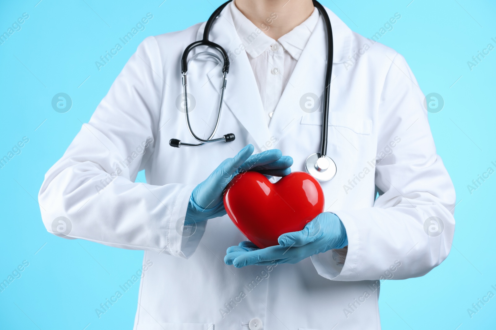 Photo of Doctor with red heart on light blue background, closeup