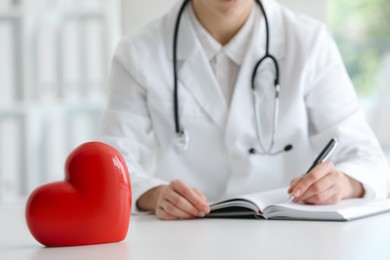 Photo of Doctor working at table in clinic, focus on red heart