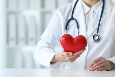 Photo of Doctor with red heart at table in clinic, closeup. Space for text