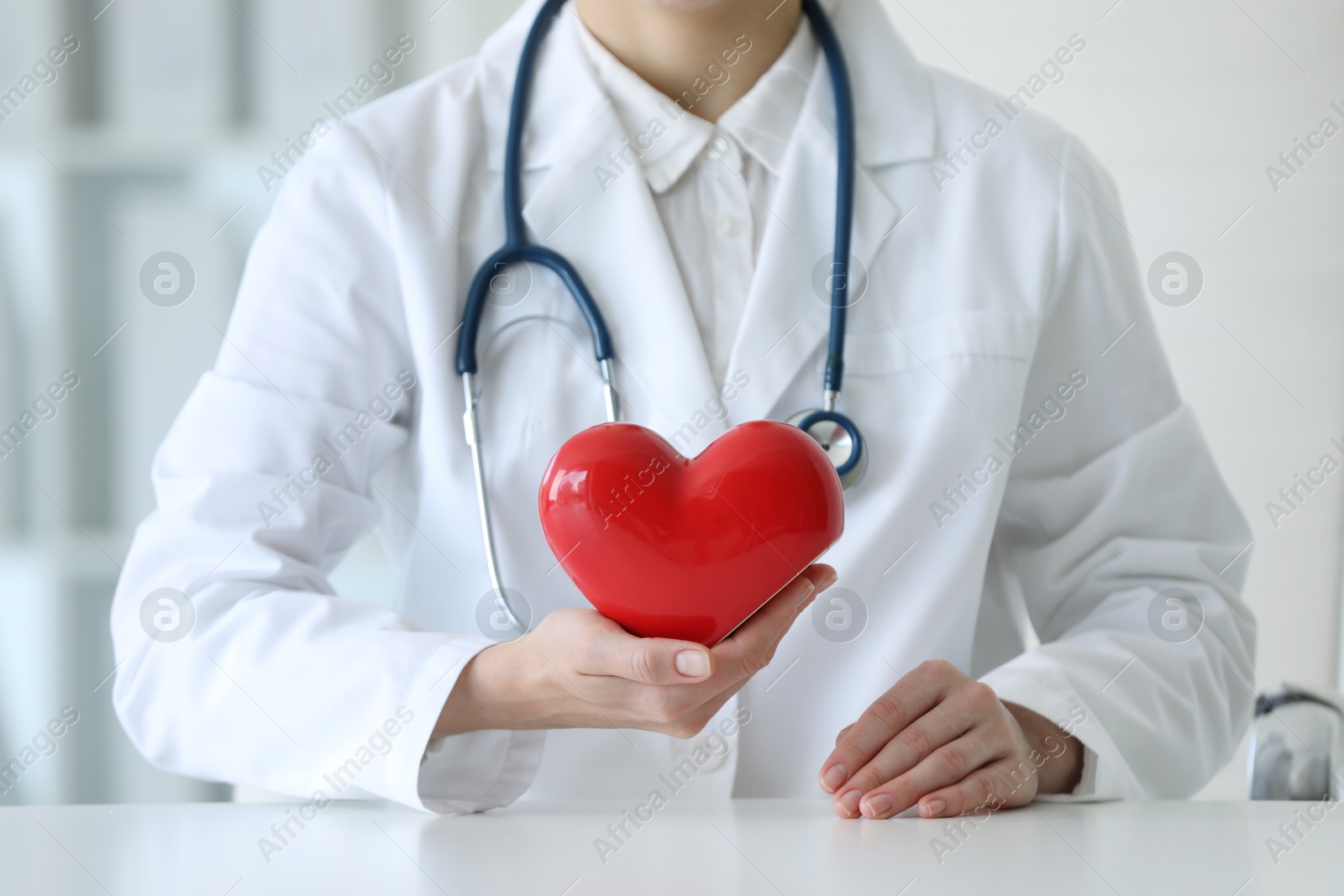 Photo of Doctor with red heart at table in clinic, closeup