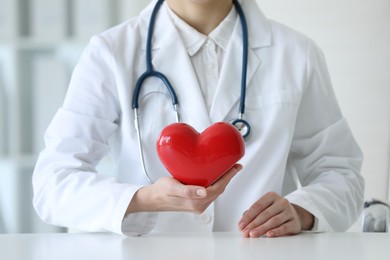 Doctor with red heart at table in clinic, closeup