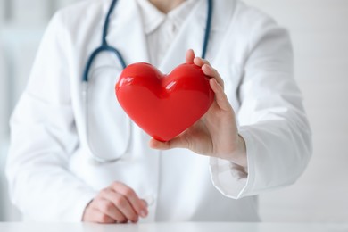 Photo of Doctor with red heart at table in clinic, closeup