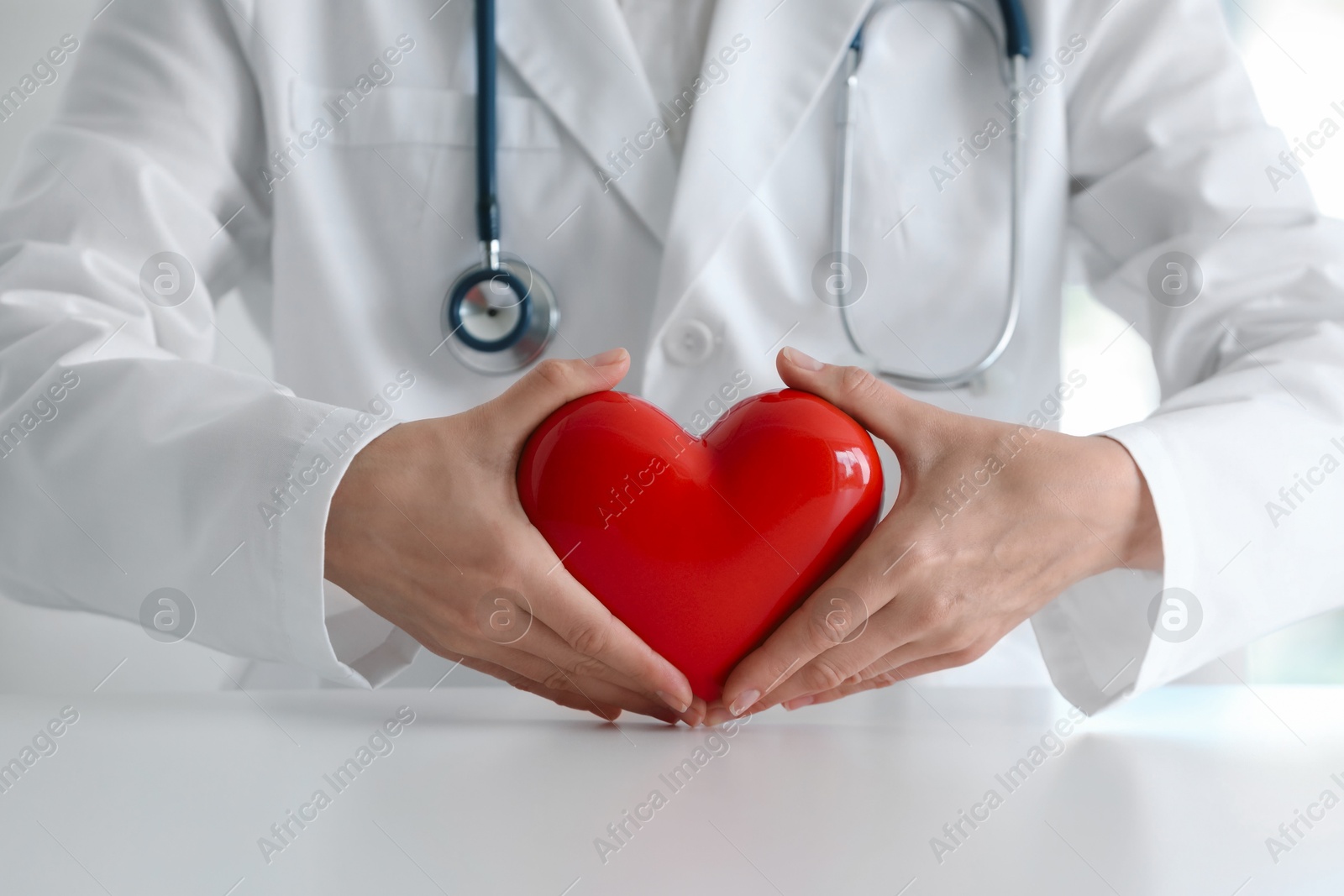 Photo of Doctor with red heart at table in clinic, closeup