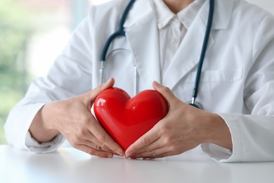 Doctor with red heart at table in clinic, closeup