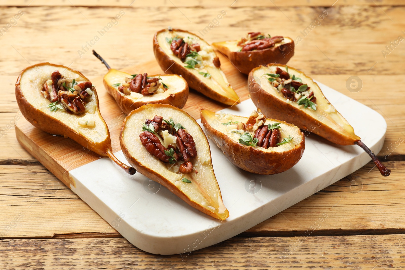 Photo of Tasty baked pears with nuts, blue cheese, thyme and honey on wooden table