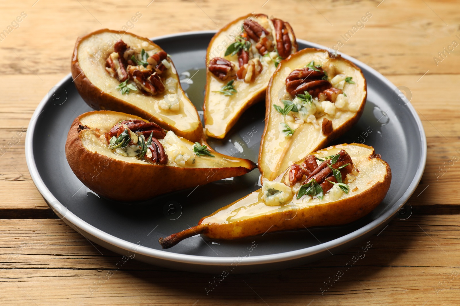 Photo of Tasty baked pears with nuts, blue cheese, thyme and honey on wooden table