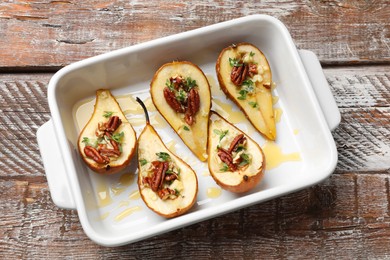 Tasty baked pears with nuts, blue cheese, thyme and honey in baking dish on wooden table, top view