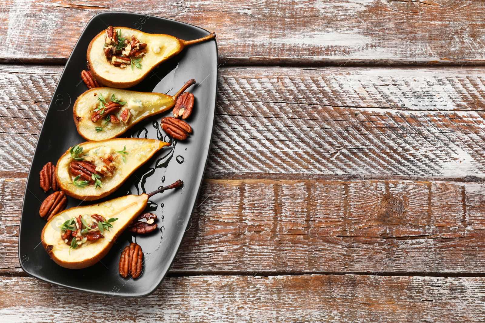 Photo of Tasty baked pears with nuts, blue cheese, thyme and honey on wooden table, top view. Space for text