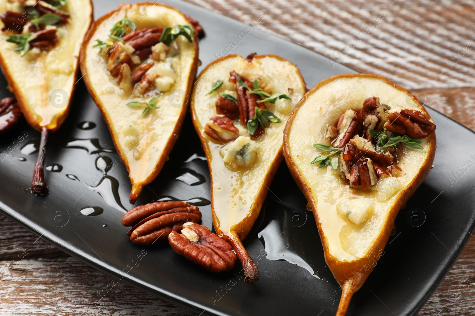 Photo of Tasty baked pears with nuts, blue cheese, thyme and honey on wooden table, closeup