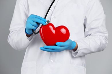 Doctor with stethoscope and red heart on grey background, closeup