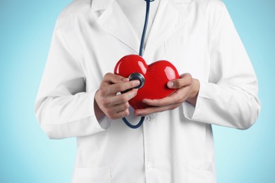 Doctor with stethoscope and red heart on light blue background, closeup