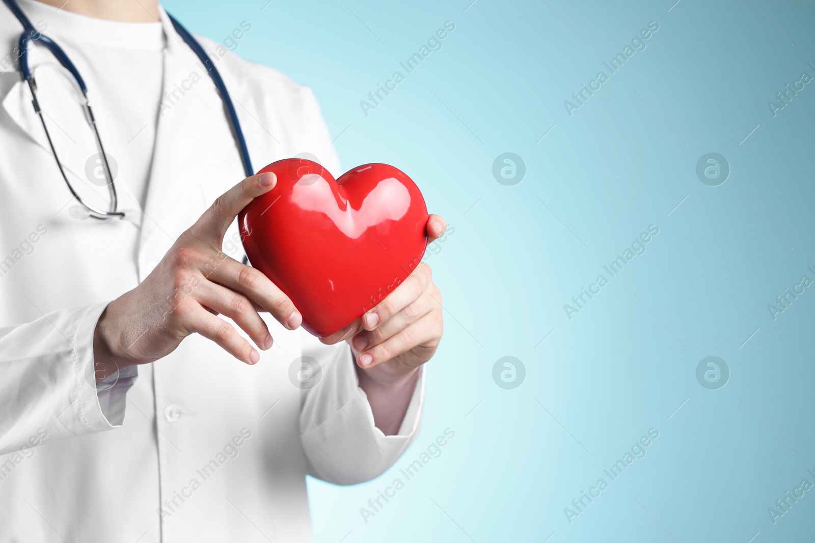 Photo of Doctor with red heart on light blue background, closeup. Space for text