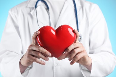 Doctor with red heart on light blue background, selective focus