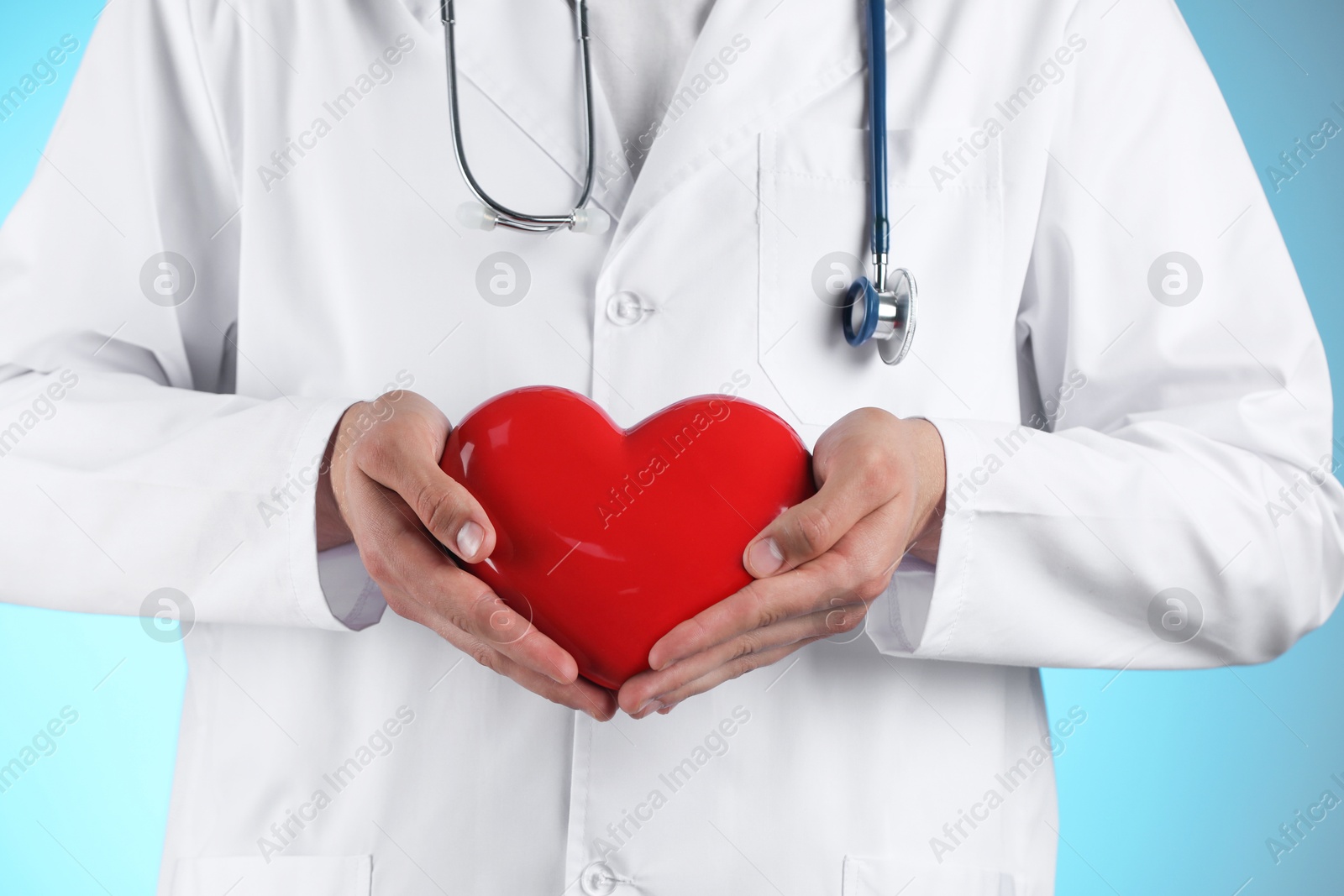 Photo of Doctor with red heart on light blue background, closeup