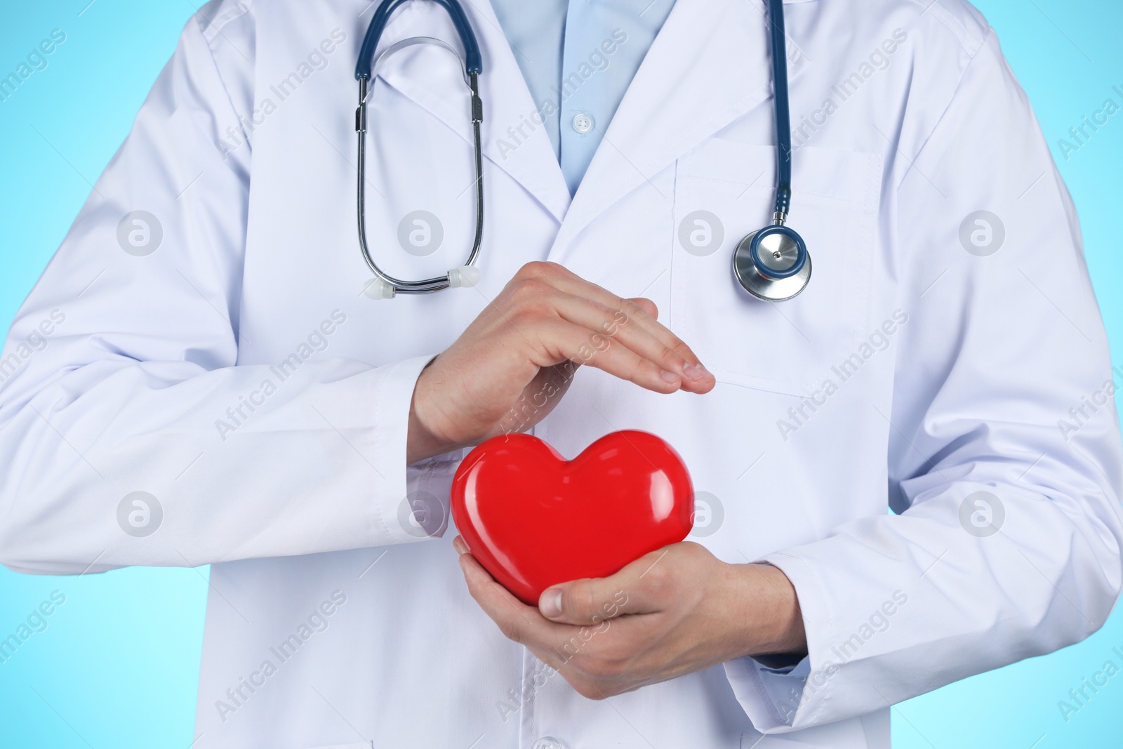 Photo of Doctor with red heart on light blue background, closeup