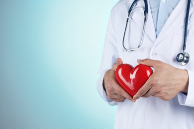 Photo of Doctor with red heart on light blue background, closeup. Space for text