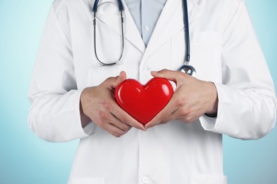 Photo of Doctor with red heart on light blue background, closeup