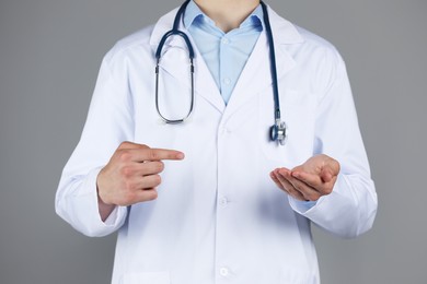 Photo of Doctor pointing at something on grey background, closeup