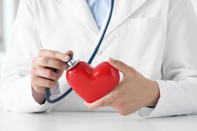 Doctor with stethoscope and red heart at white table, closeup