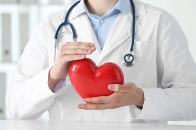 Doctor with red heart at white table in clinic, closeup