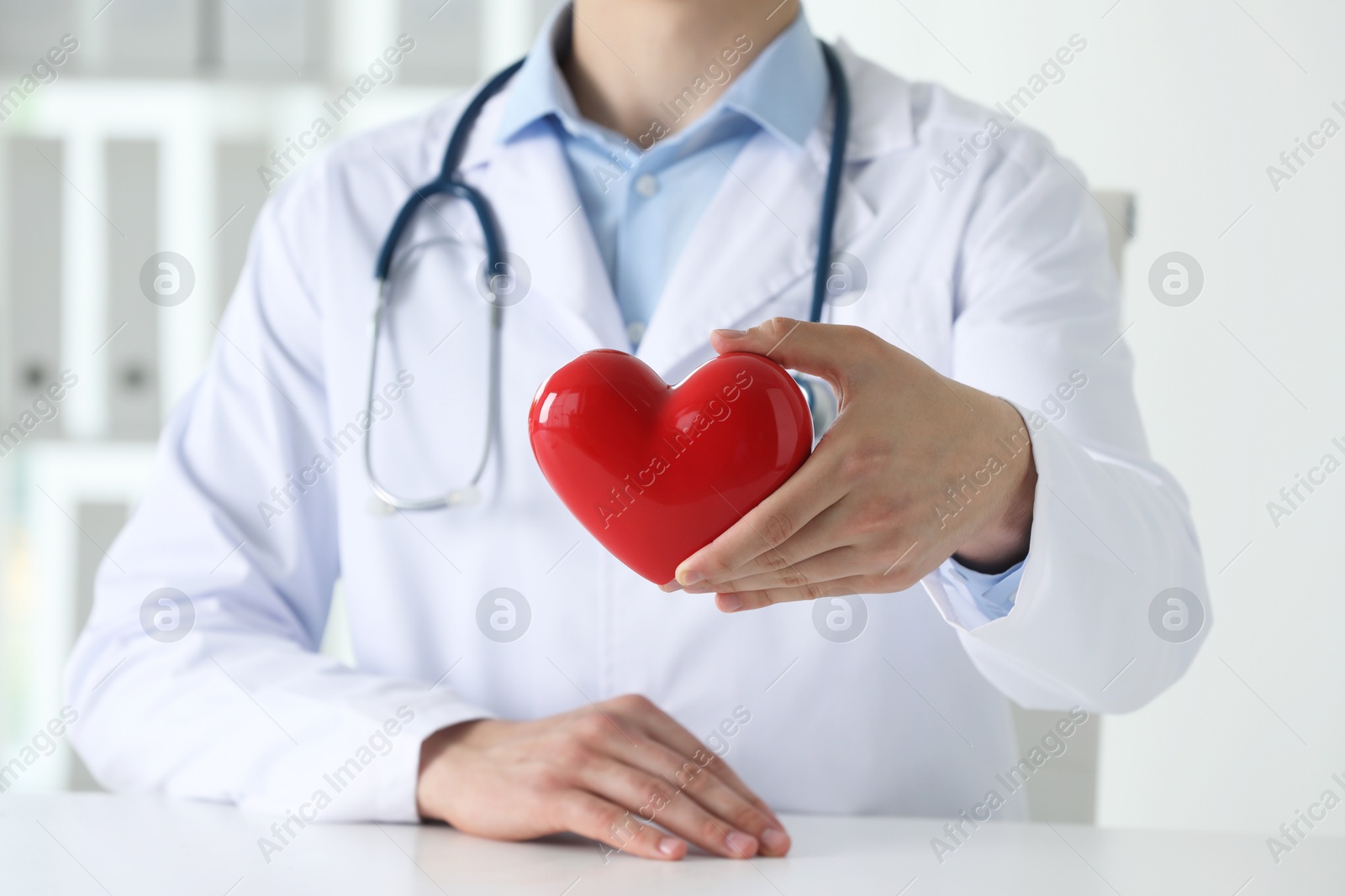 Photo of Doctor with red heart at white table in clinic, closeup