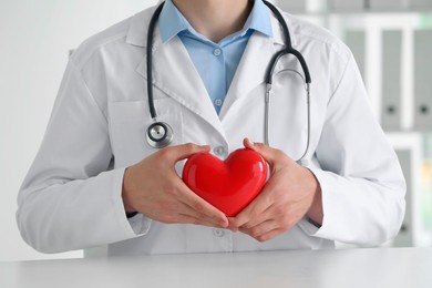 Photo of Doctor with red heart at white table in clinic, closeup