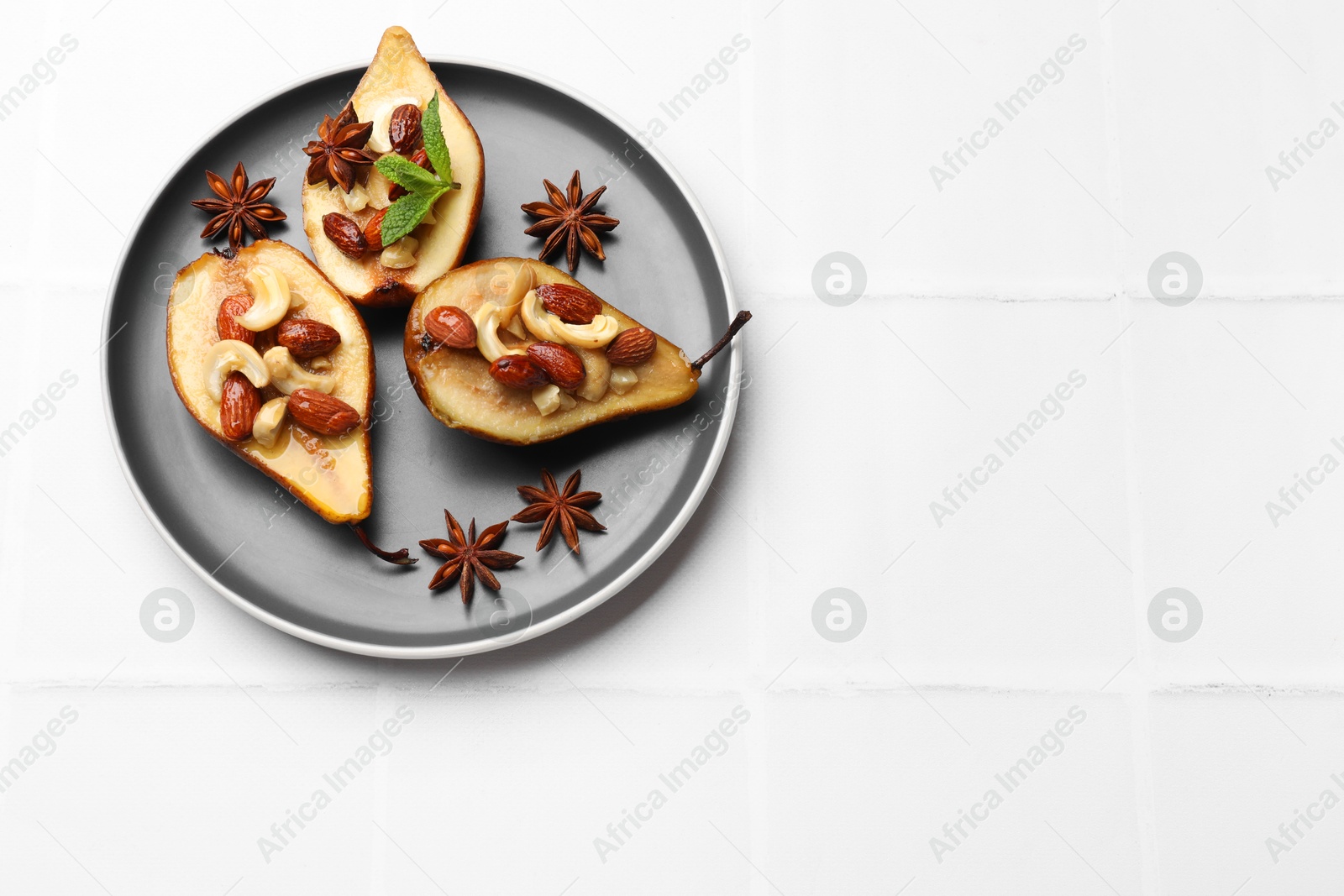 Photo of Delicious baked pears with nuts and anise stars on white tiled table, top view. Space for text