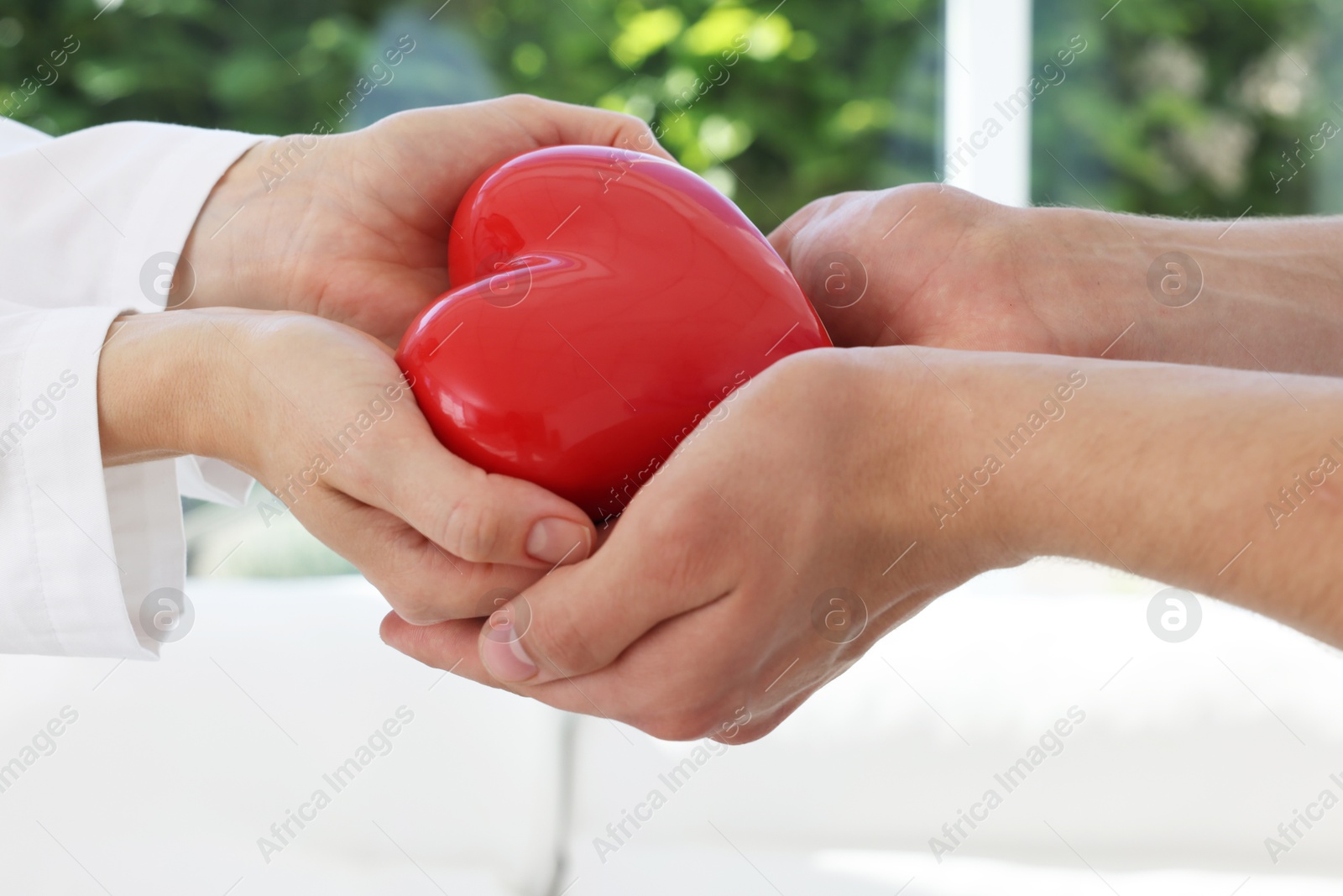 Photo of Doctor giving red heart to patient at white table in clinic, closeup