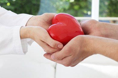 Photo of Doctor giving red heart to patient at white table in clinic, closeup