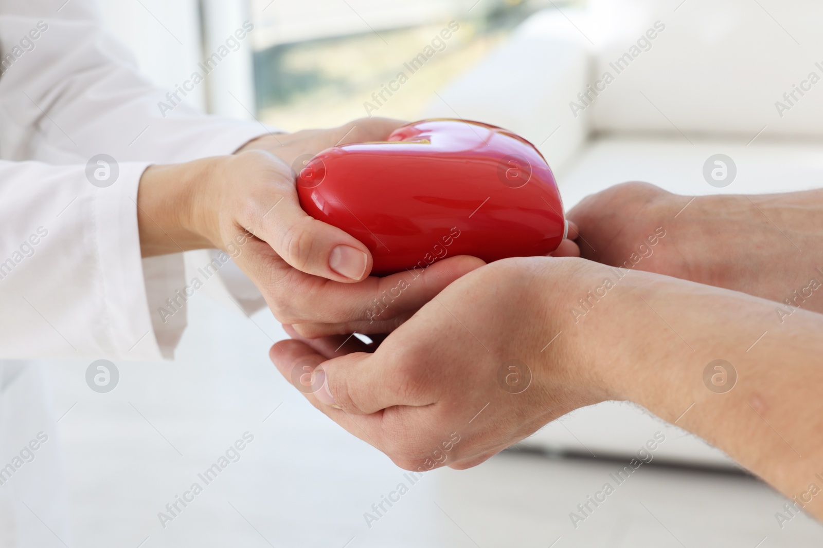 Photo of Doctor giving red heart to patient at white table in clinic, closeup