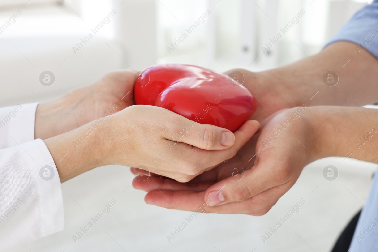 Photo of Doctor giving red heart to patient at white table in clinic, closeup