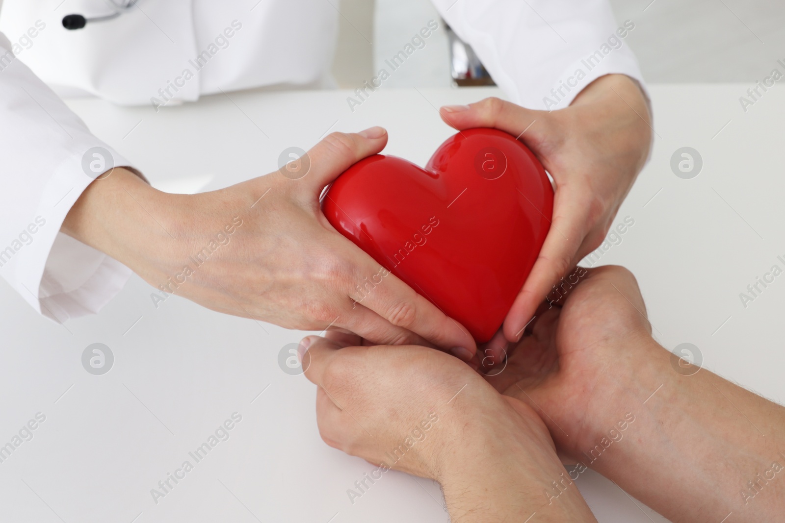 Photo of Doctor giving red heart to patient at white table in clinic, closeup