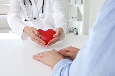 Photo of Doctor showing red heart to patient at white table in clinic, closeup