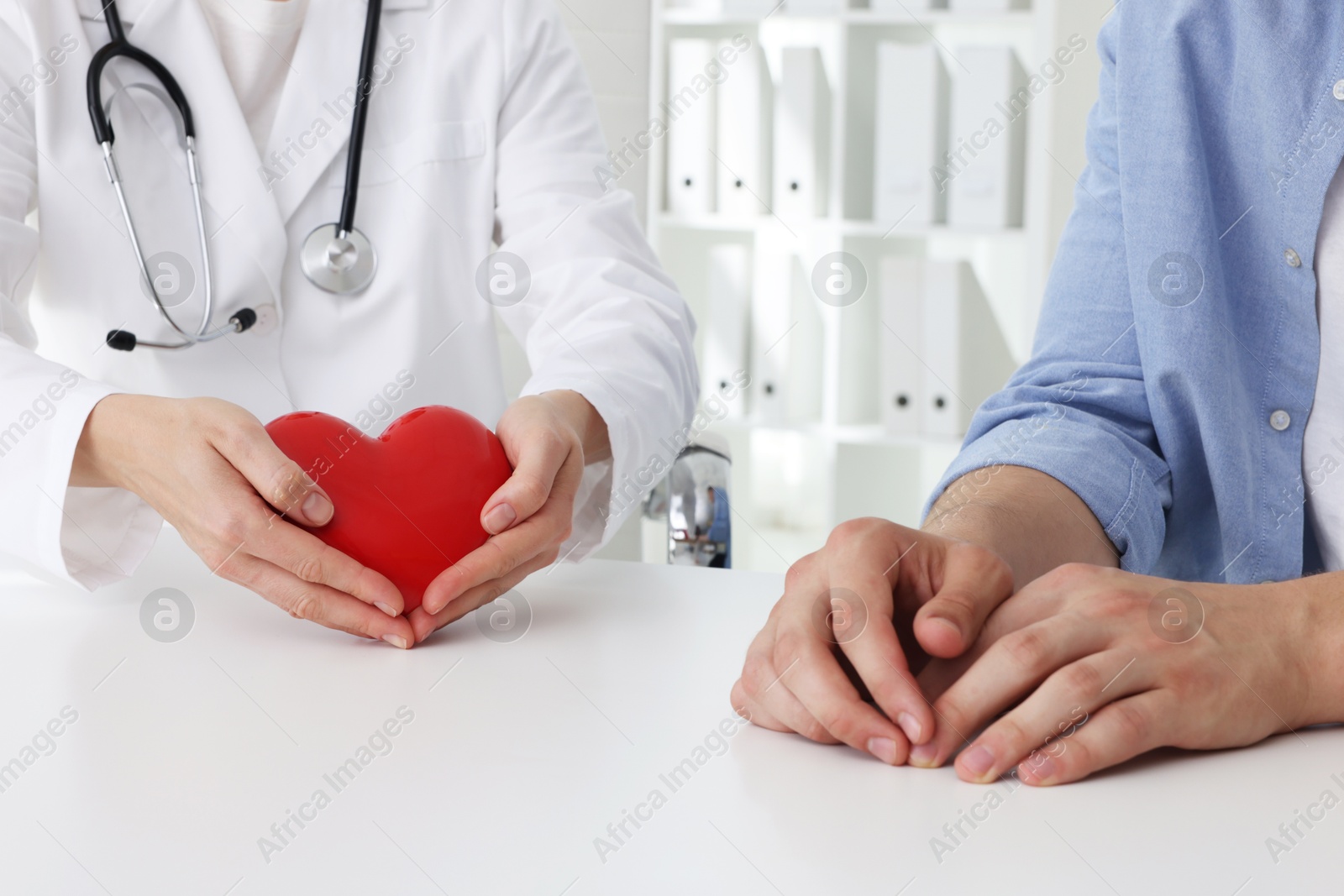 Photo of Doctor showing red heart to patient at white table in clinic, closeup