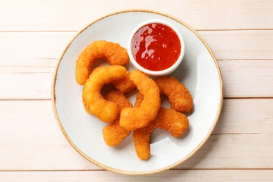 Photo of Tasty breaded fried shrimps and sauce on light wooden table, top view