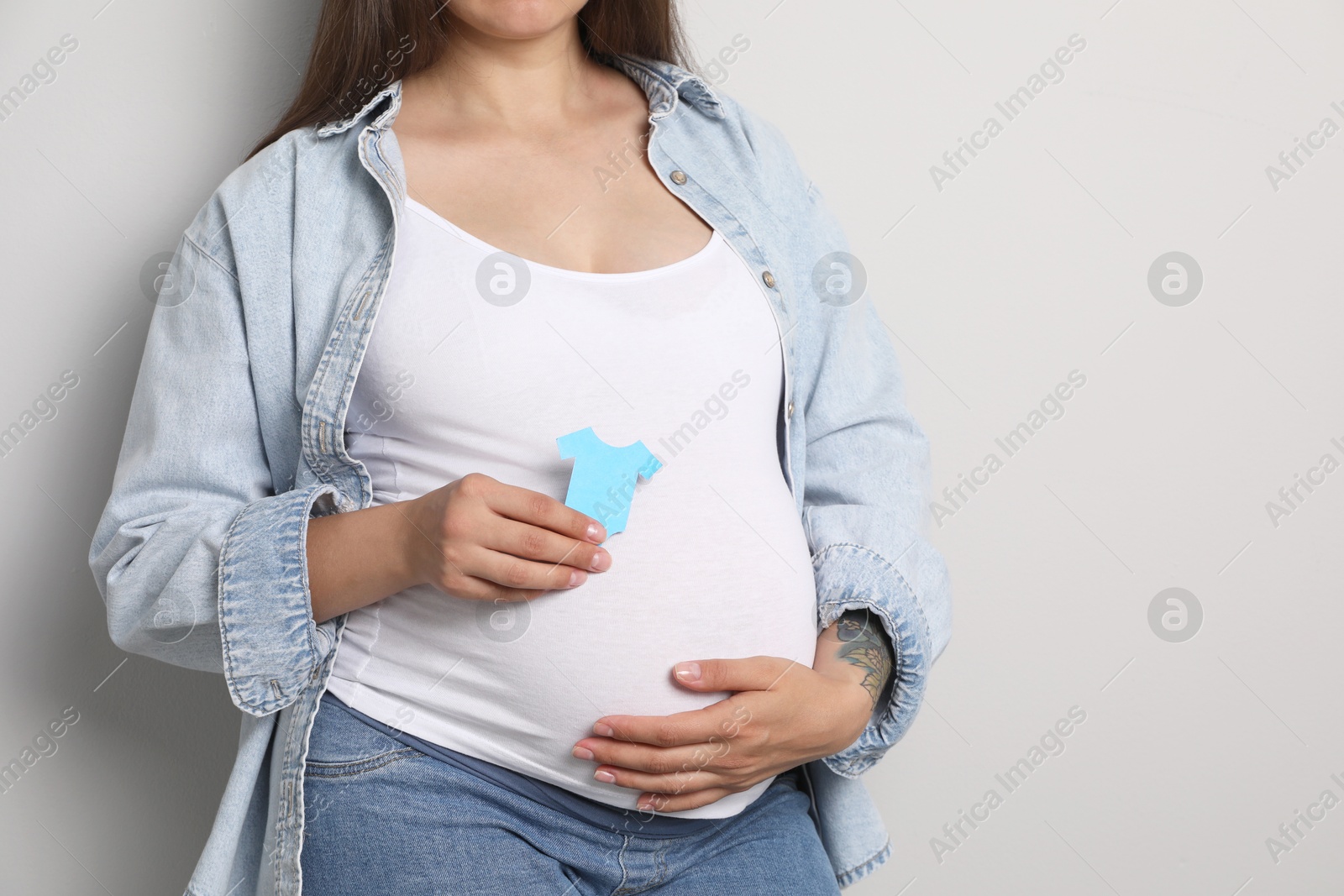 Photo of Pregnant woman with light blue paper T-shirt on gray background, closeup. Space for text