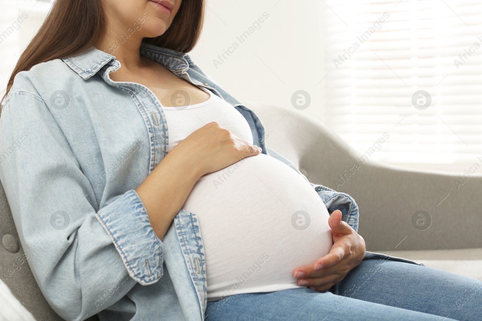 Photo of Pregnant woman sitting on sofa at home, closeup