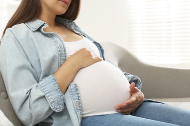 Photo of Pregnant woman sitting on sofa at home, closeup