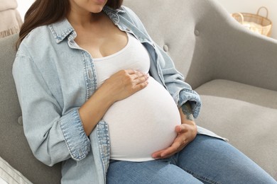 Photo of Pregnant woman sitting on sofa at home, closeup