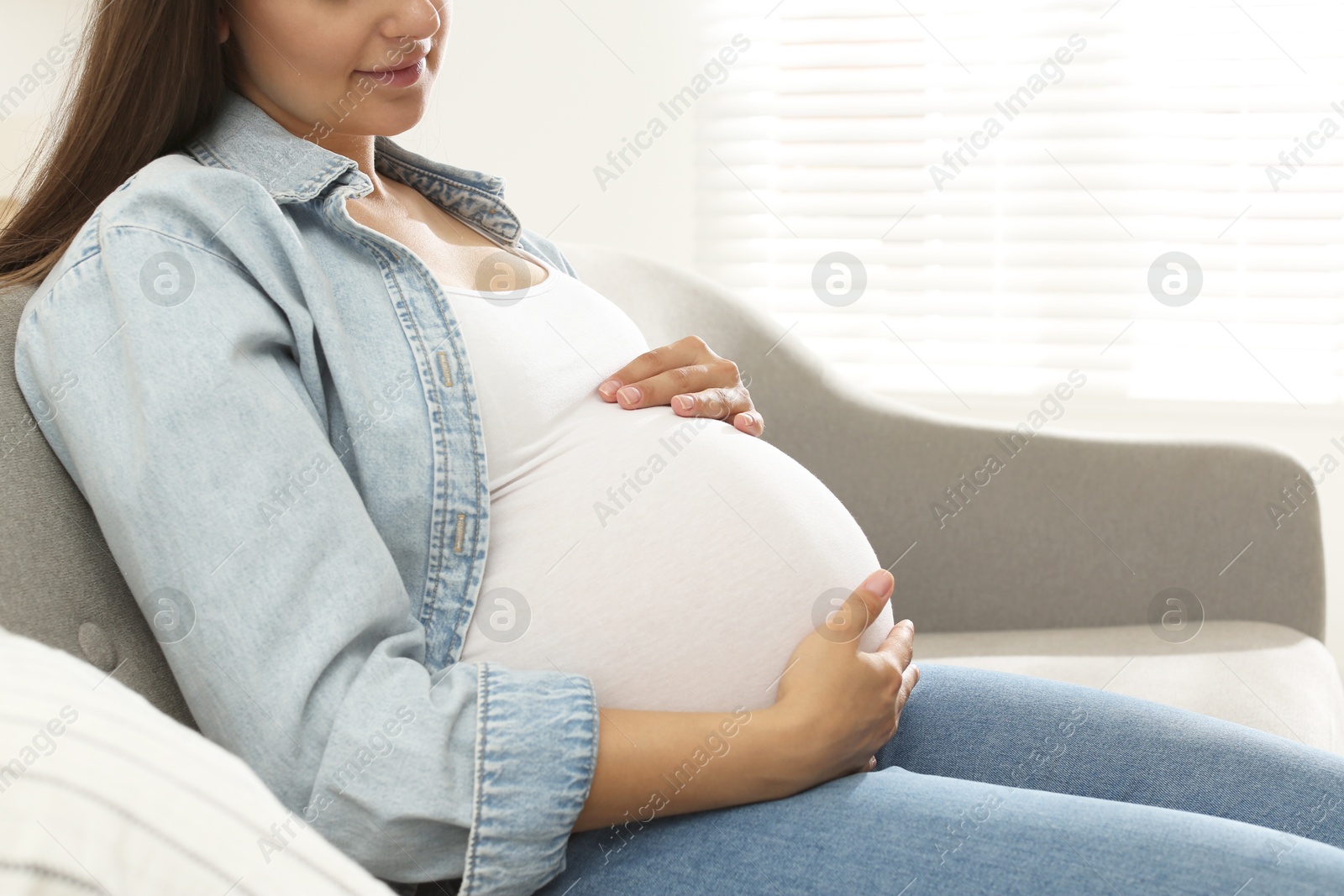 Photo of Pregnant woman sitting on sofa at home, closeup