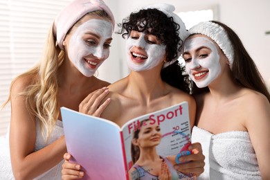 Happy friends with facial masks reading magazine in bathroom. Spa party