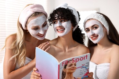 Photo of Happy friends with facial masks reading magazine in bathroom. Spa party