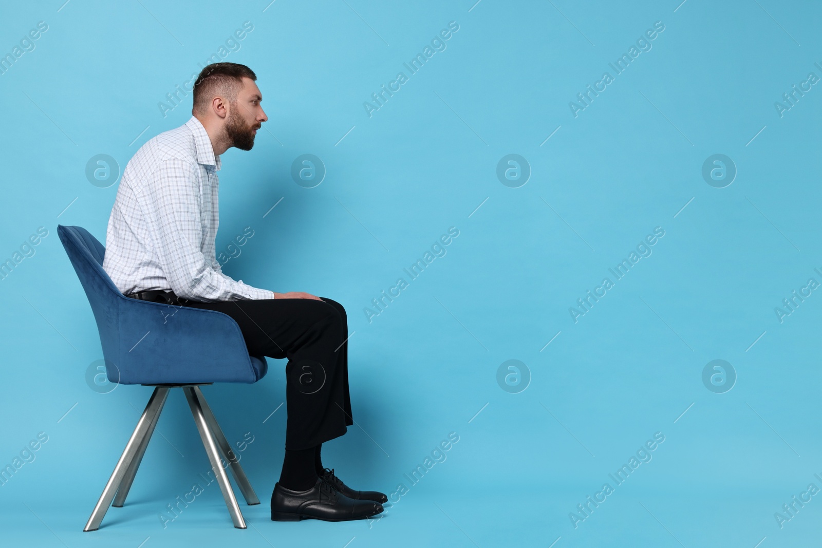 Photo of Man with poor posture sitting on chair against light blue background, space for text