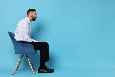 Photo of Man with poor posture sitting on chair against light blue background, space for text